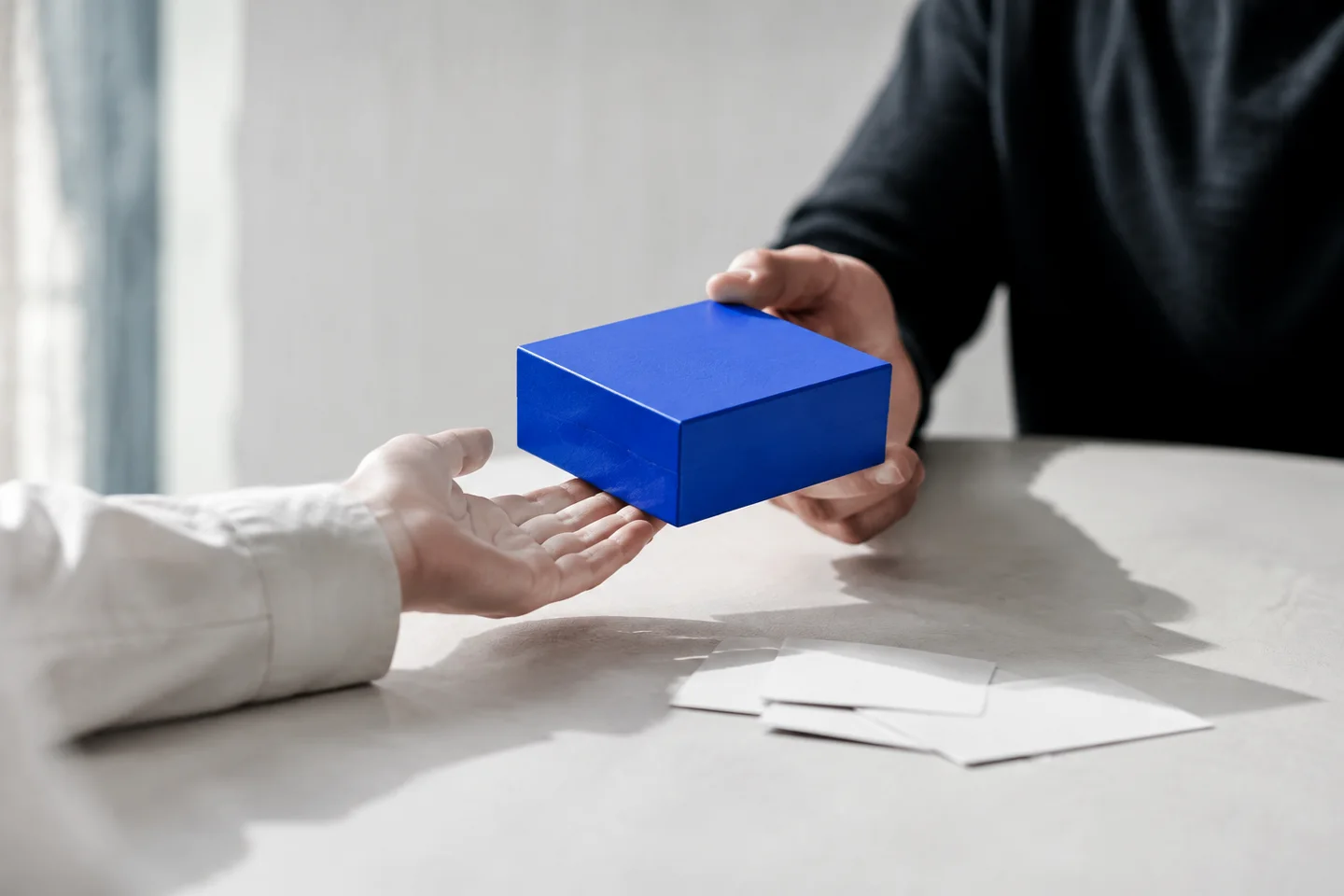 Hands passing a cobalt-blue product box across a table.
