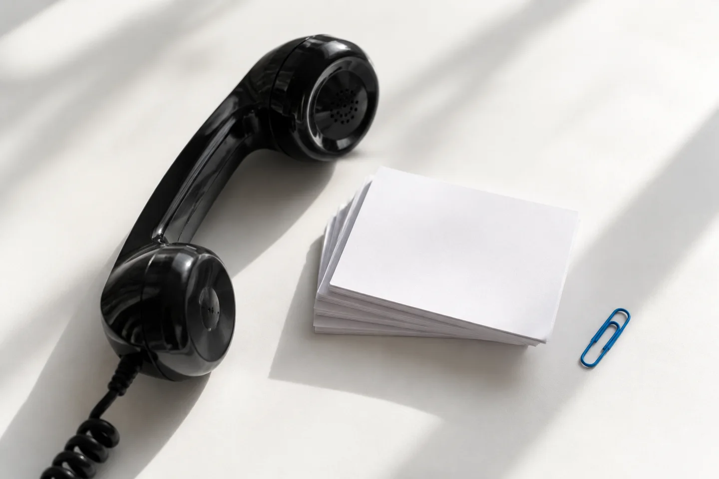 Black telephone handset beside blank context cards and a blue paperclip.
