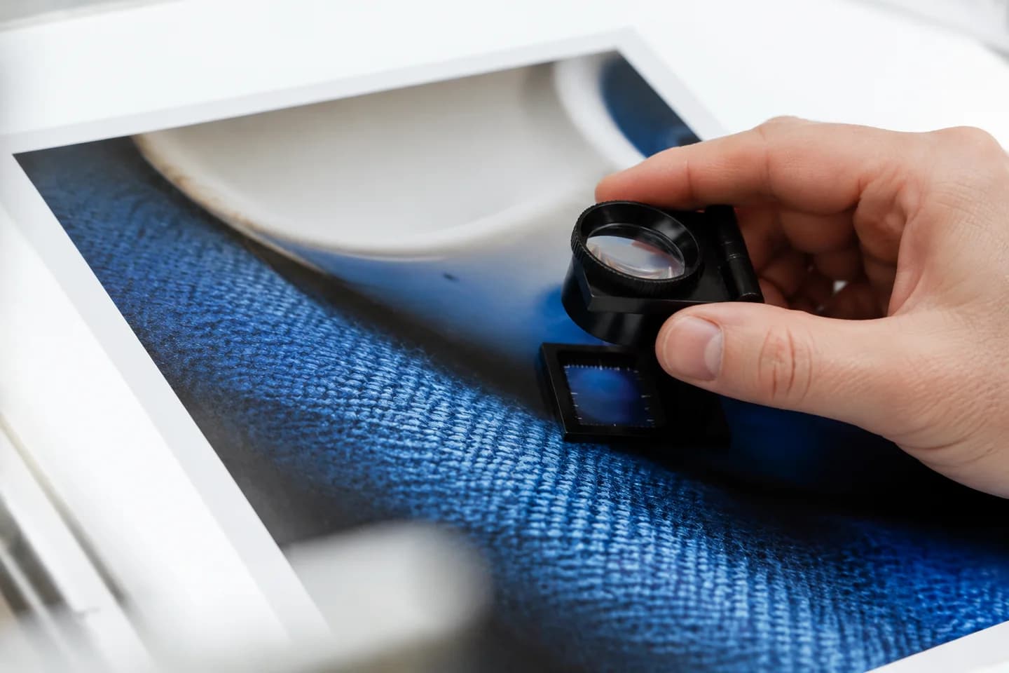 A magnifying loupe inspecting fine fabric and ceramic detail in a photograph.